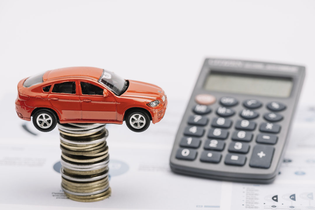 Pilha de moedas com miniatura de carro equilibrada e calculadora sobre planilha de cálculos