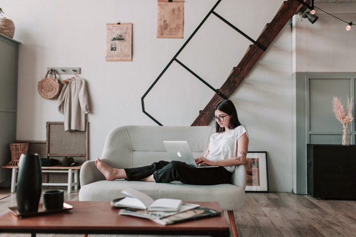 Mulher sentada em sofá digitando em notebook em ambiente moderno e casual