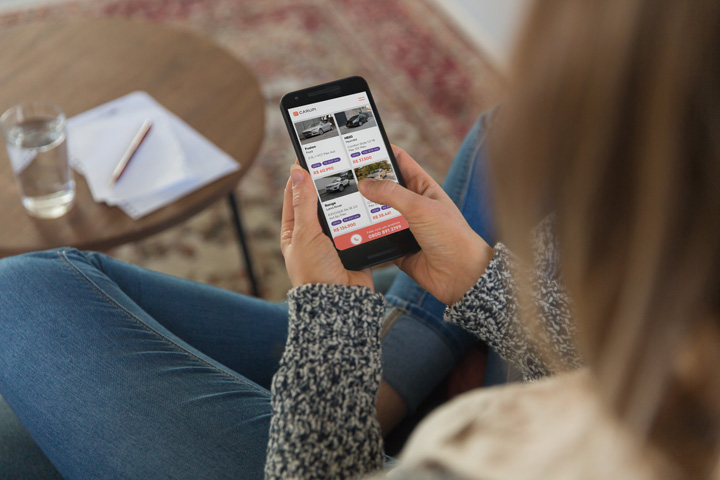 Mulher sentada em sofá de casa acessando website CARUPI em seu celular
