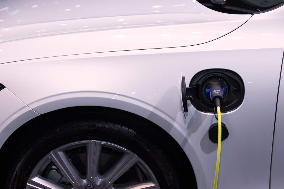 Close em carro elétrico branco com cabo de energia plugado em tomada de carga