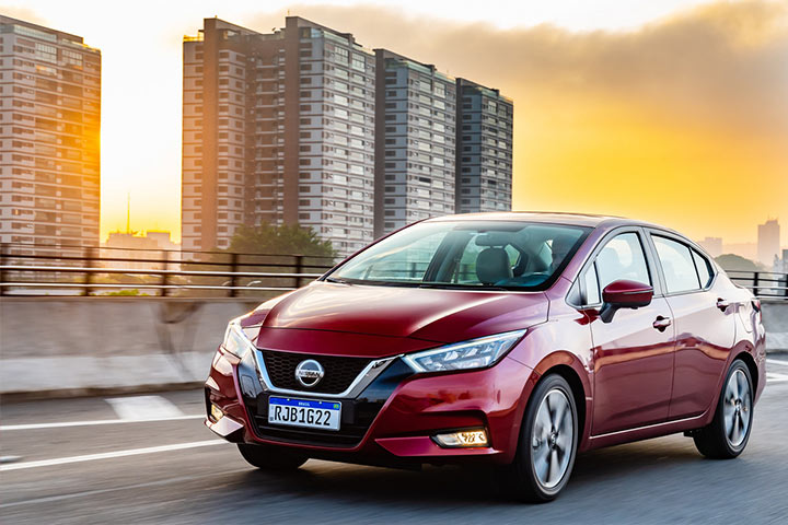 Nissan Versa V-Drive em viaduto de cidade grande com prédios e entardecer ao fundo