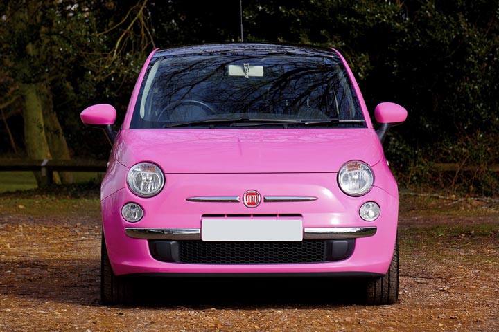 Carro Fiat 500 de cor rosa choque estacionado debaixo de arvoredo