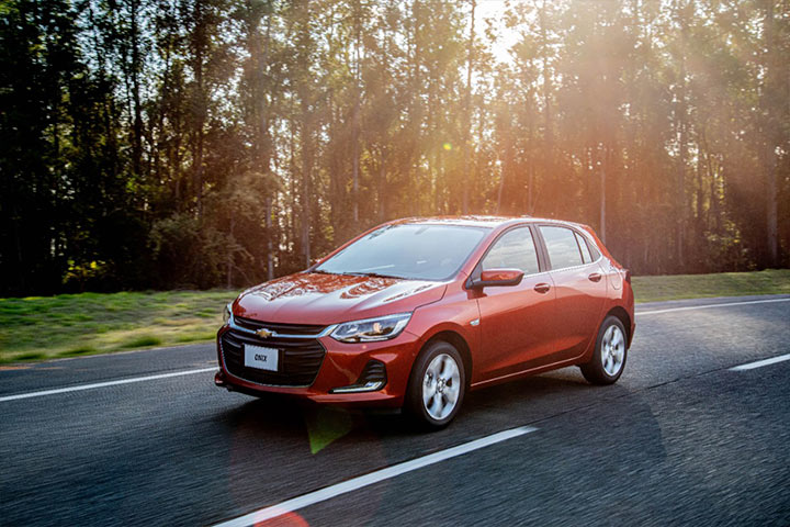 Chevrolet Onix circulando por rodovia arborizada durante entardecer