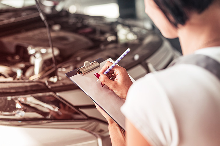 Mulher realizando vistoria automotiva segurando prancheta com carro ao fundo