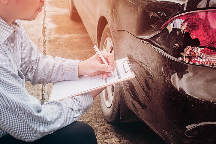 Homem com prancheta checando traseira de carro de perto durante vistoria veicular