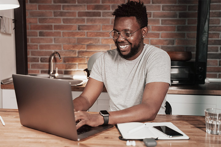 Rapaz sorridente usando laptop em sua casa e comprando carros online na CARUPI