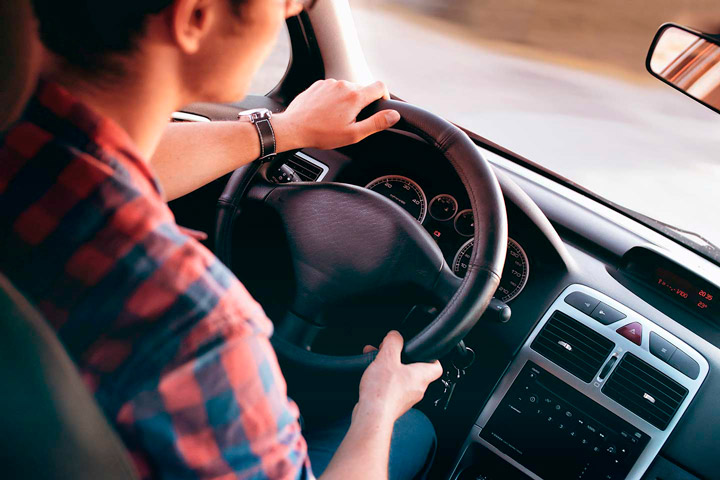 Rapaz dirigindo carro com mãos no volante visto do banco traseiro