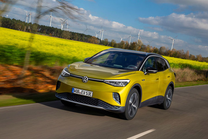 Volkswagen ID.4 amarelo trafegando em rodovia rural com geradores de energia eólica ao fundo