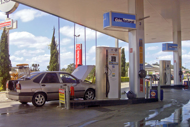 Carro estacionado em posto de abastecimento GNV com capô e porta-malas abertos
