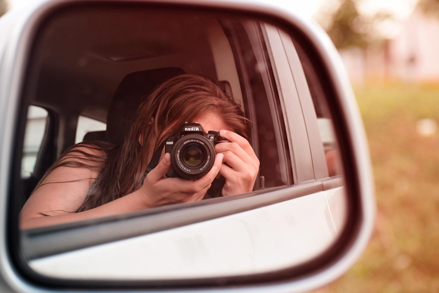 Mulher dentro de carro com câmera fotográfica fotografando retrovisor do veículo que reflete sua imagem