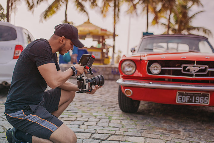 Rapaz fotografando Ford Mustang vermelho em calçada à beira-mar