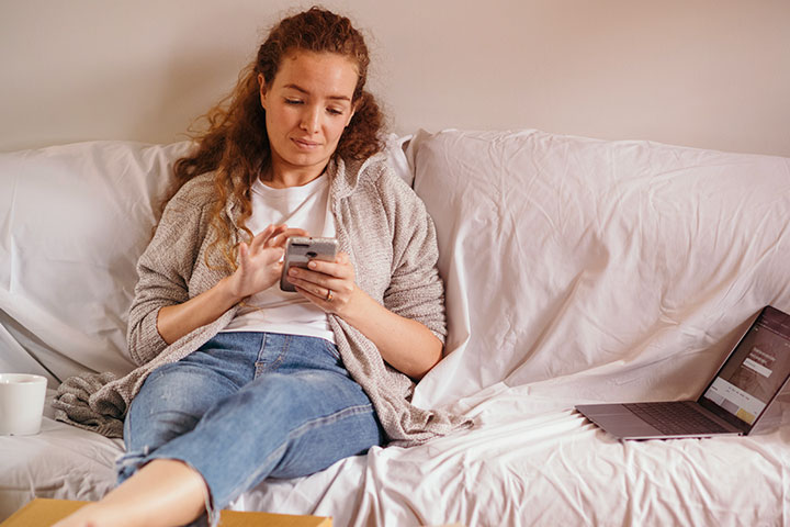 Jovem mulher ruiva sentada relaxadamente em sofá acessando plataforma da CARUPI em seu celular
