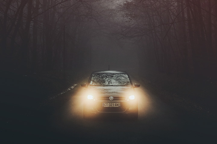 Vista frontal de carro trafegando em estrada ao anoitecer com luzes acesas