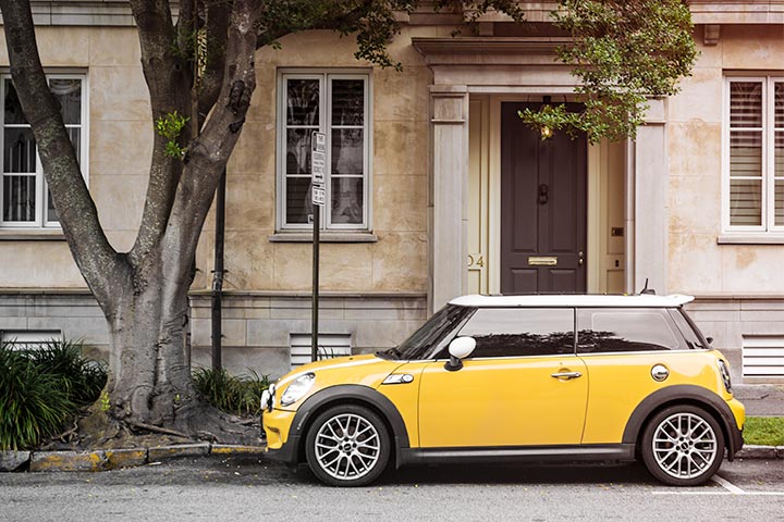Mini Cooper amarelo estacionado em frente a casa antiga debaixo de árvore frondosa