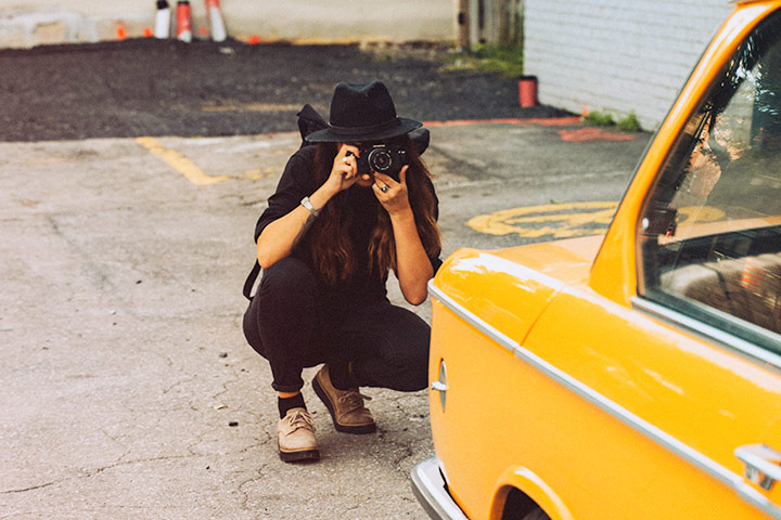 Jovem mulher agachada com câmera fotográfica para fotografar carro antigo amarelo