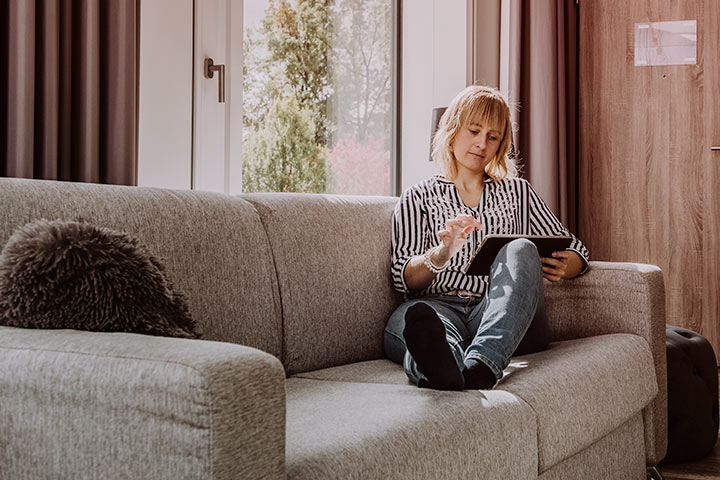 Mulher relaxando em sofá da sala enquanto acessa site da CARUPI em seu tablet