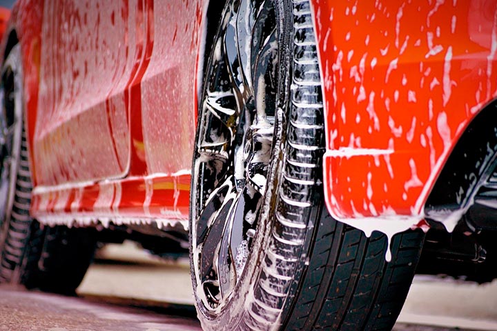 Close em rodas de carro vermelho sendo lavado, com espuma escorrendo pela carroceria