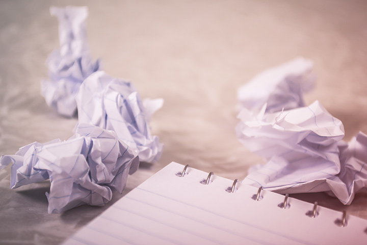 Folhas de papel amassadas com más ideias e caderno de anotações