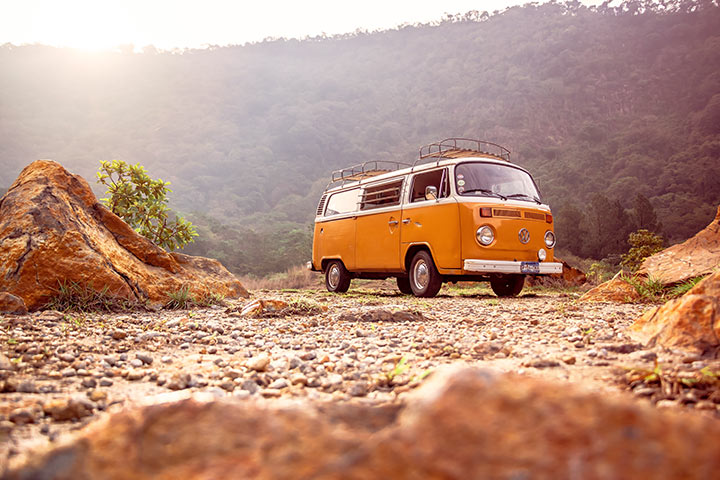 Volkswagen Kombi amarela antiga com bagageiros de teto estacionada em terreno pedregoso em cenário natural