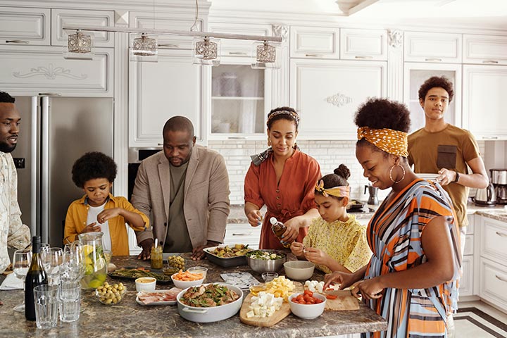 Família afro-americana com 7 membros de diferentes idades reunida ao redor de mesa da cozinha em momento descontraído