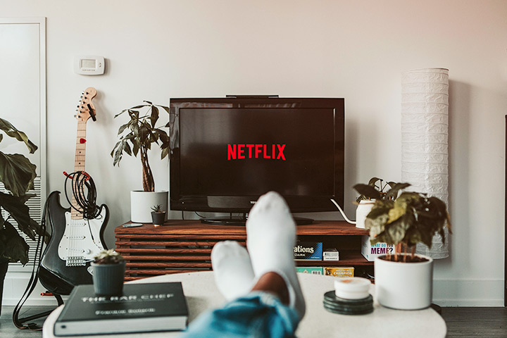 Vista do observador com pés apoiados sobre mesa de centro e televisor ligado na Netflix