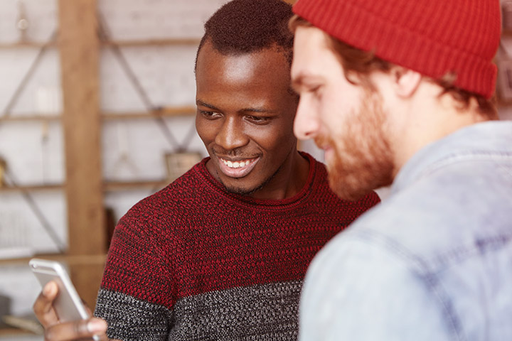 Homem Afro-americano mostrando tela de seu celular para amigo caucasiano e sorrindo