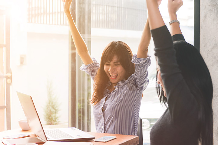 Jovens mulheres felizes e celebrando resultados com computador em mesa de trabalho