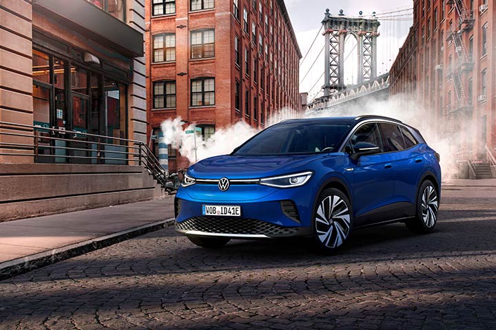 Carro elétrico ID.4 da Volkswagen na cor azul parado em rua de cidade industrial com prédios ao fundo