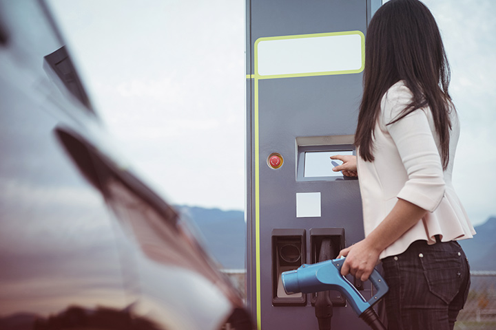 Jovem mulher segurando mangueira de carregamento de carro elétrico e configurando estação de carga