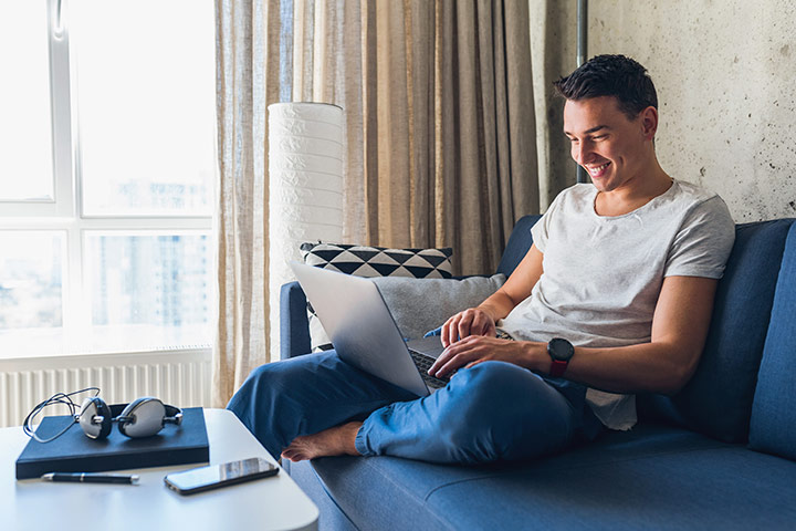 Rapaz sorridente em sofá de sua casa acessando website da Carupi para comprar carros usados online