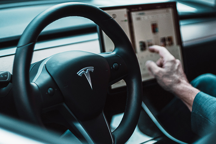 Interior de carro Tesla com volante em destaque e central multimídia ao fundo com motorista operando sistema