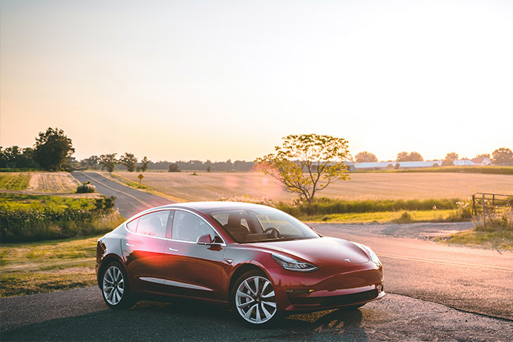 Tesla Model 3 estacionado em acostamento de estrada rural com luz do sol da tarde iluminando sua pintura