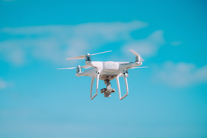 Drone branco com quatro hélices voando com céu azul ao fundo