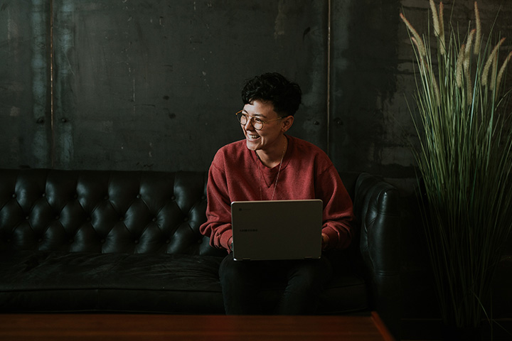 Jovem mulher sentada em sofá de couro vintage de estilo inglês acessando Carupi em seu notebook