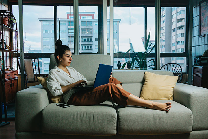 Jovem mulher relaxando no sofá de sua casa e acessando plataforma da Carupi em seu notebook