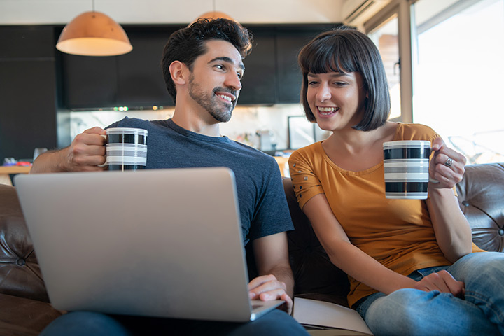 Jovem casal relaxando em sofá de casa e acessando website da Carupi para comprar carros usados online