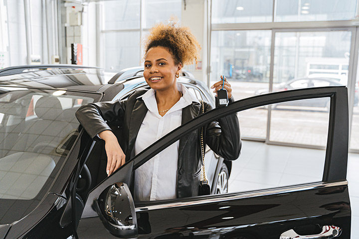 Jovem mulher afro-americana sorrindo ao segurar a chave de seu carro novo em concessionária de veículos