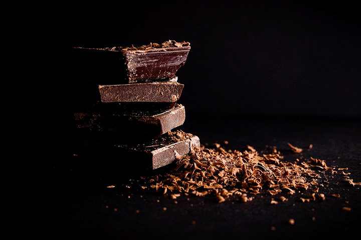 Barras de chocolate meio amargo empilhadas e raspas de chocolate ao lado em cenário escuro