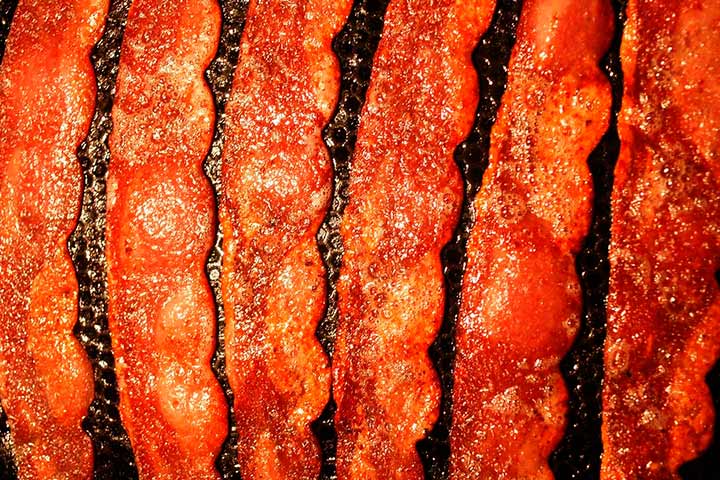 Fatias de bacon em fritura com borbulhas de óleo na chapa