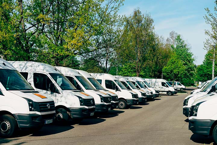 Pátio de empresa com frota de vans estacionada lado a lado e árvores ao fundo
