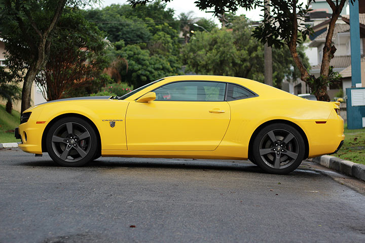 Chevrolet Camaro amarelo estacionado em rua pacata com casas e árvores