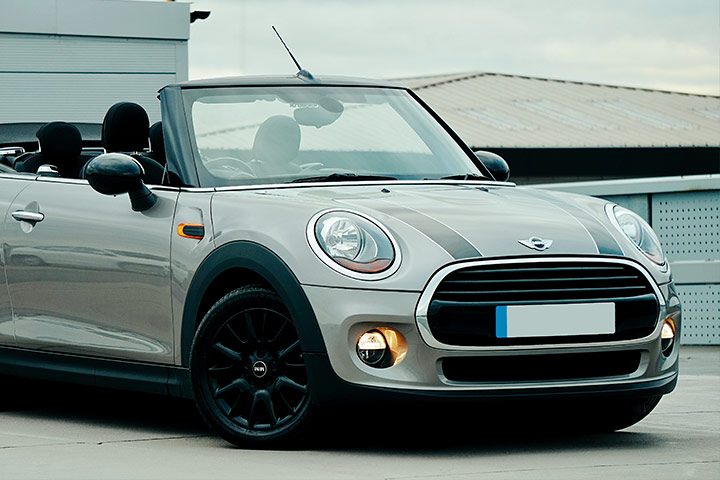 Mini Cooper conversível estacionado em área aberta com construções ao fundo