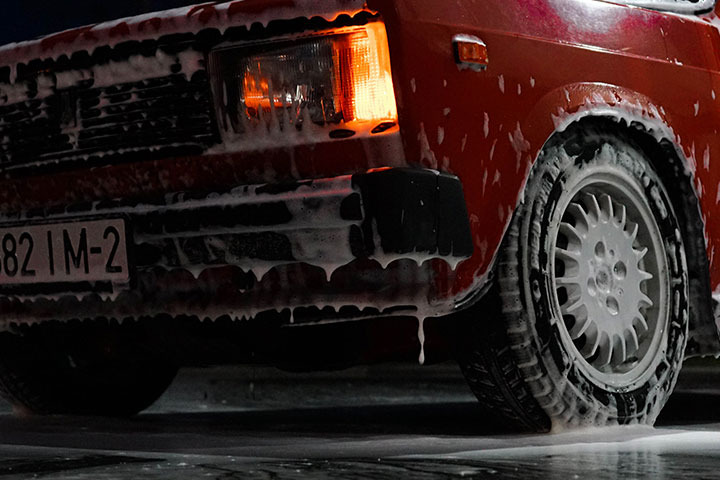 Carro antigo de cor vermelha com farol acesso e espuma de sabão escorrendo por toda a lataria
