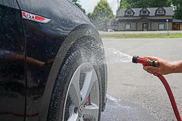 Lateral dianteira de carro da Volkswagen recebendo esguicho de mangueira durante lavagem de carro