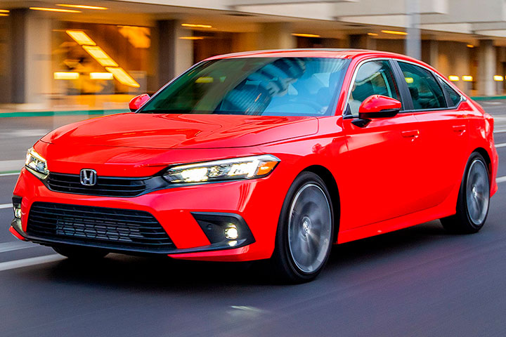 Honda Civic 2022 vermelho trafegando em rua urbana com lojas iluminadasao fundo