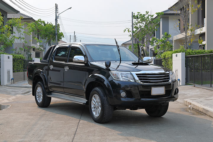 Toyota Hilux preta estacionada de forma transversal em rua tranquila de bairro suburbano