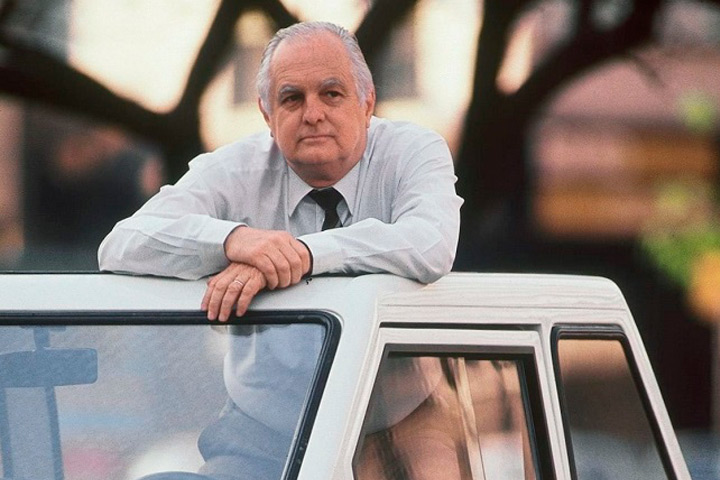 João Amaral Gurgel, fundador da Gurgel Motores, desbruçado sobre um de seus carros e olhando para o alto