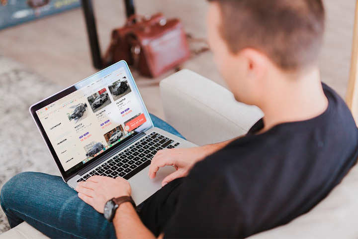 Jovem rapaz sentado em sofá com notebook no colo acessando website da Carupi
