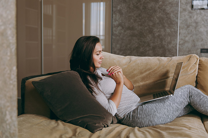 Jovem mulher sentada confortavelmente em sofá de casa com laptop no colo acessando website Carupi