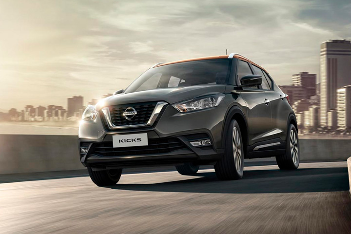 Nissan Kicks cinza com teto laranja visto de frente trafegando em via urbana com cidade e mar ao fundo
